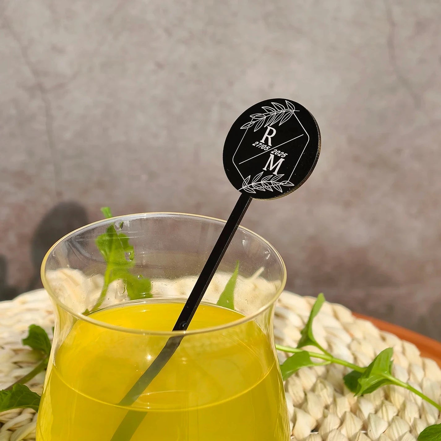 Glass of yellow liquid with a black straw and decorative sticker on a textured surface.