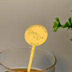 Gold drink marker with personalized text in a glass against a neutral background