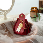 Red leather pouch with a gold bow and tag on a white fabric background