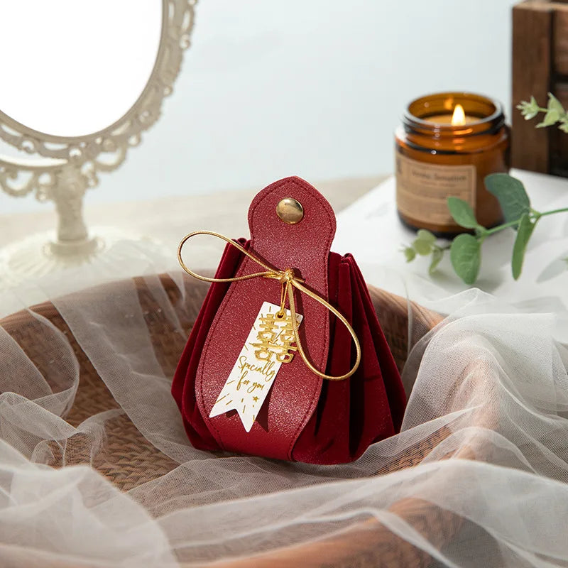 Red leather pouch with a gold bow and tag on a white fabric background