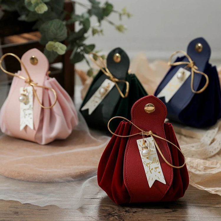 Red fabric pouch with a gold tag on a wooden surface, surrounded by other colorful pouches.
