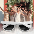 Bride in a wedding dress with bridesmaids in gold dresses, all wearing sunglasses, with a large pair of sunglasses in the foreground.