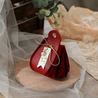 Red handbag with a gold handle on a wooden surface, surrounded by light fabric and a plant.