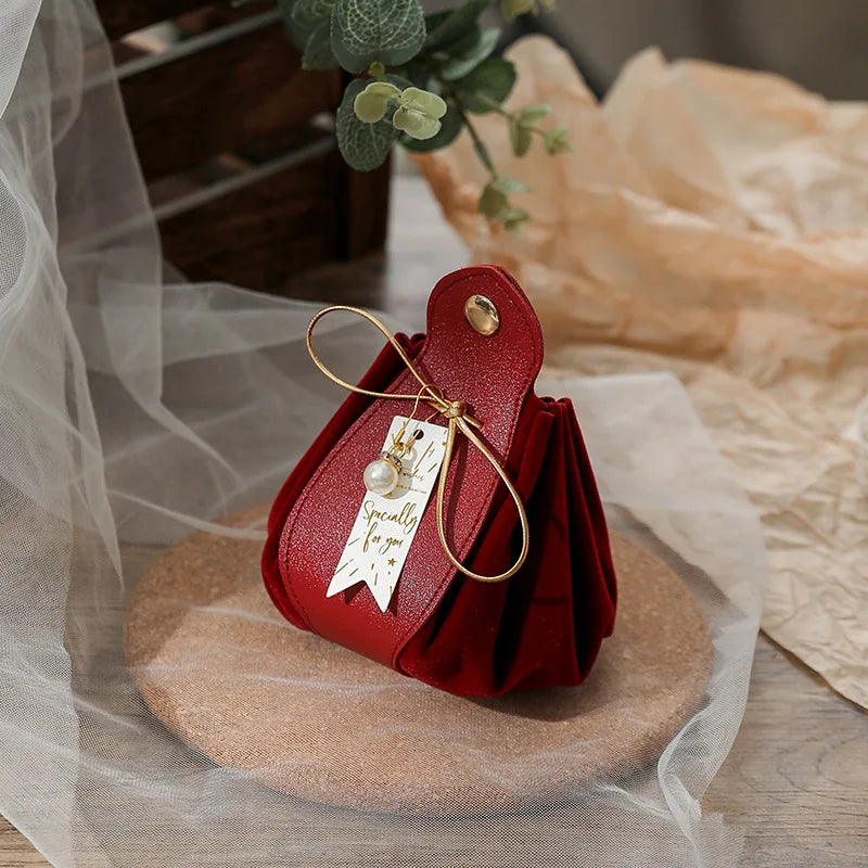 Red handbag with a gold handle on a wooden surface, surrounded by light fabric and a plant.
