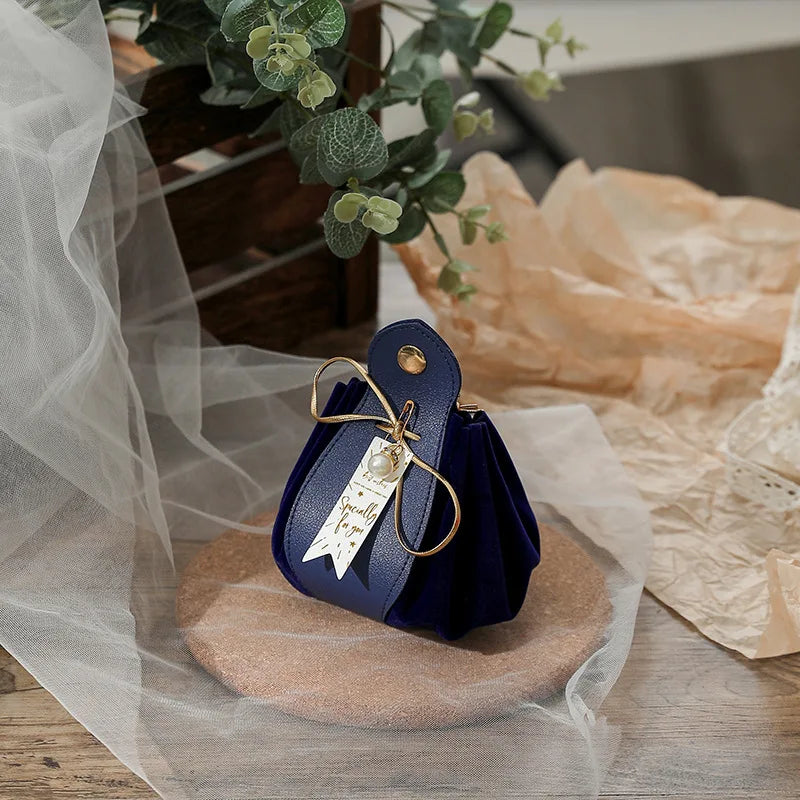 Navy blue pouch with a gold tag on a wooden surface with a plant and tissue paper in the background